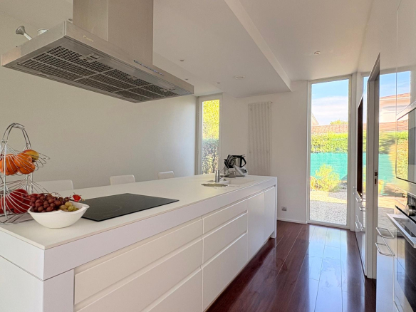 Cuisine moderne avec îlot central et vue sur la piscine, maison d'architecte au Taillan-Médoc.