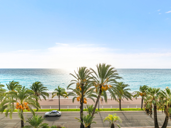 Vue panoramique sur la mer Méditerranée depuis un étage élevé à Nice, avec des palmiers au premier plan.