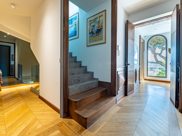 Intérieur d'une maison rénovée avec un escalier en bois et des portes en bois, vue sur un couloir lumineux.