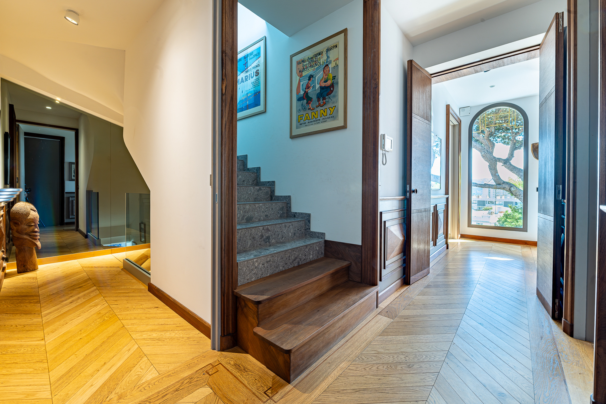 Intérieur d'une maison rénovée avec un escalier en bois et des portes en bois, vue sur un couloir lumineux.