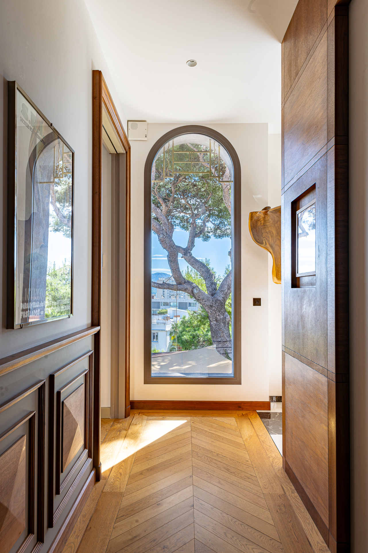Intérieur d'une maison rénovée avec un grand vitrage et un arbre visible à l'extérieur.