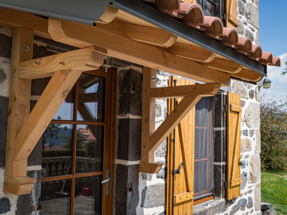 Architectural detail of a renovated old stone farmhouse with a wooden awning in Olloix.