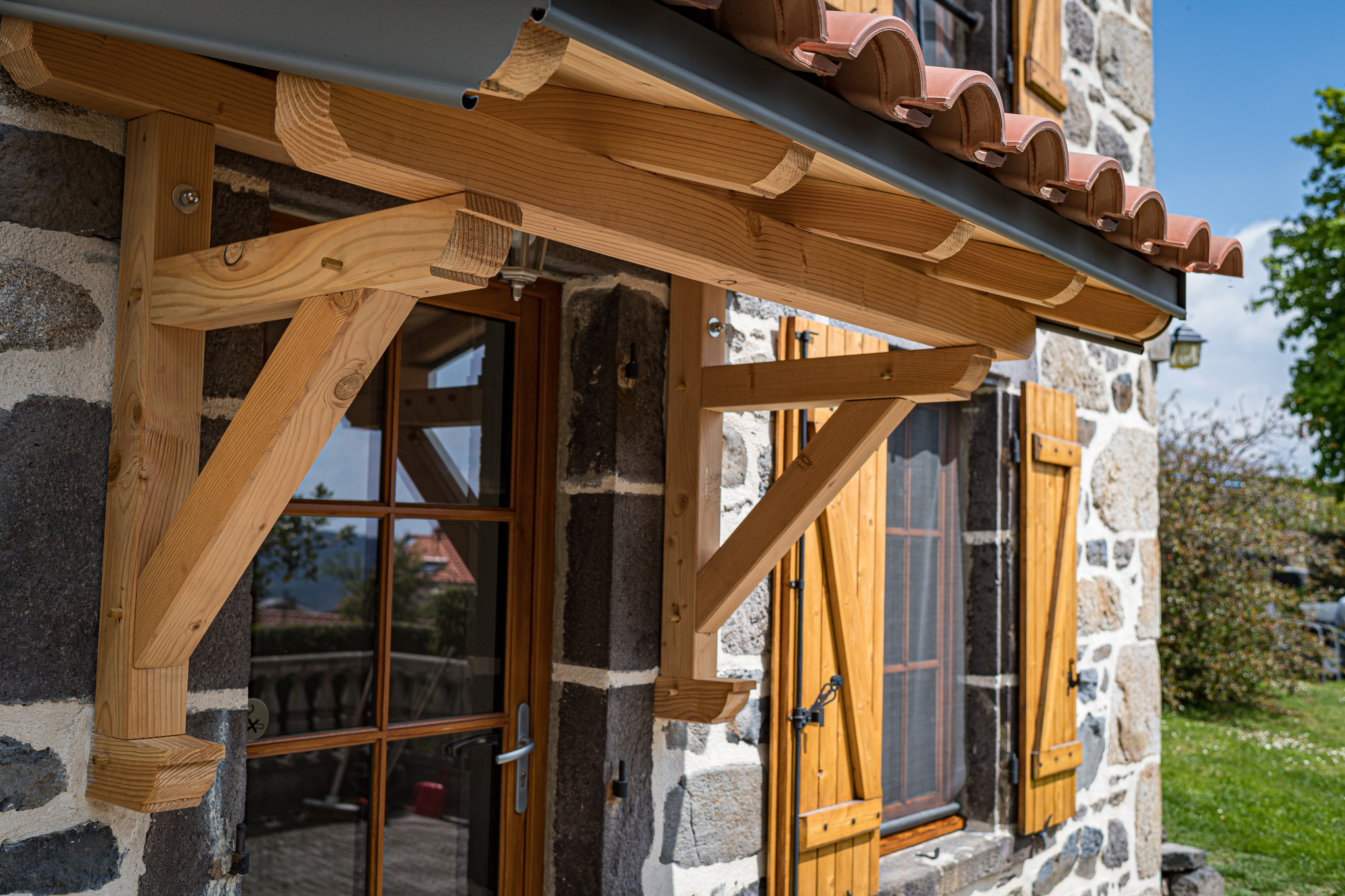 Architectural detail of a renovated old stone farmhouse with a wooden awning in Olloix.