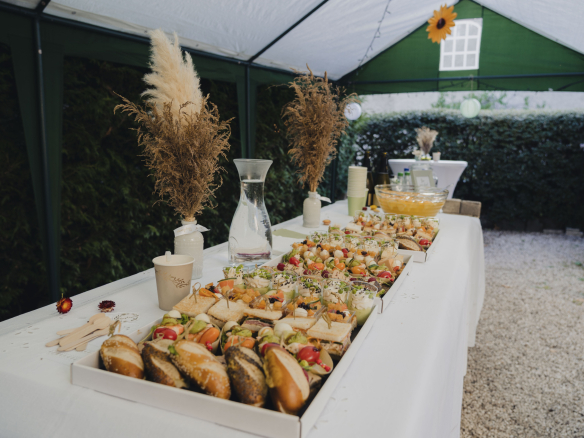 A buffet of varied dishes arranged on a table under a marquee, with natural decorations.