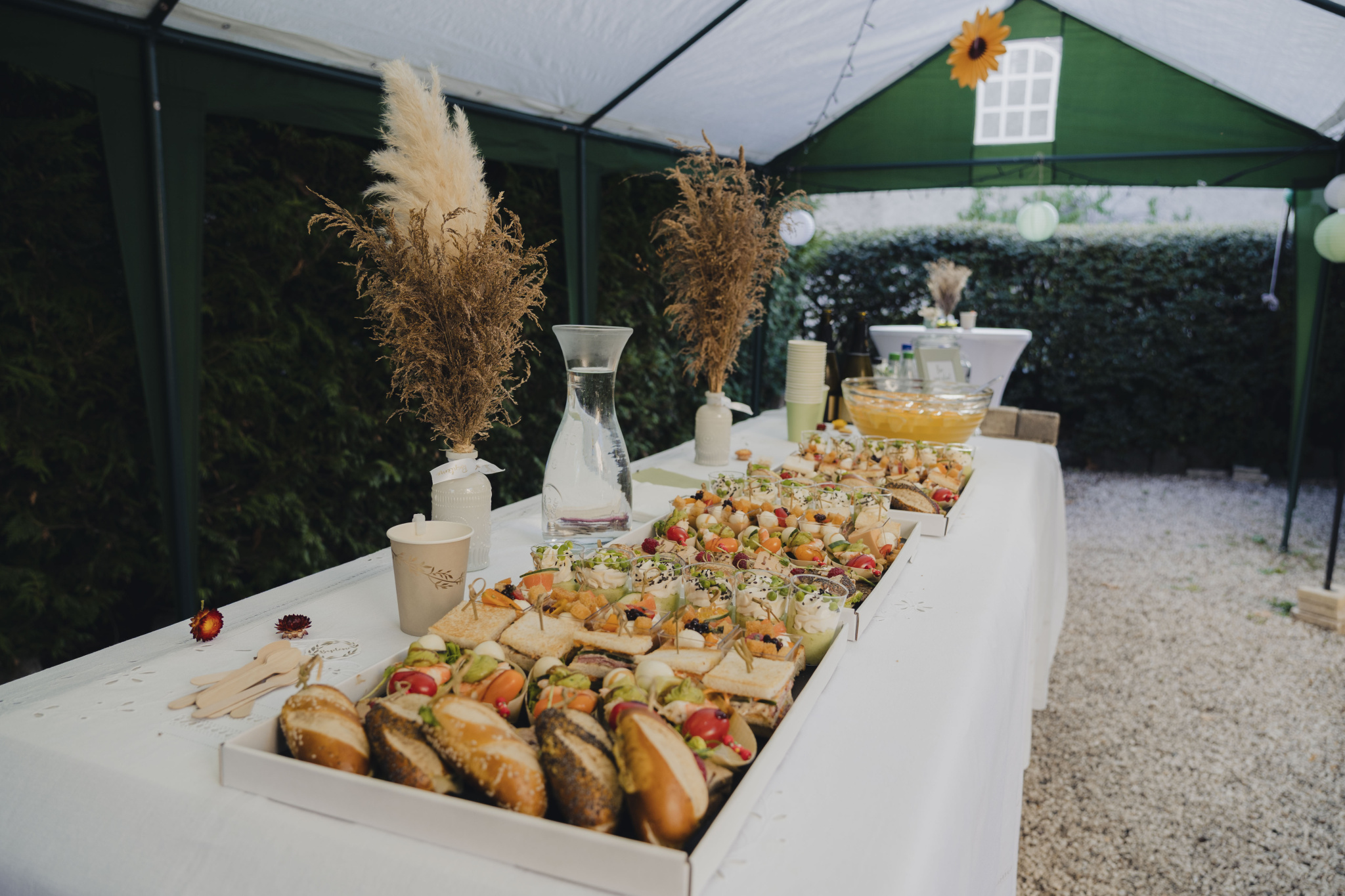 A buffet of varied dishes arranged on a table under a marquee, with natural decorations.