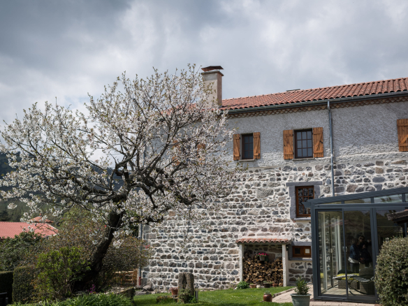 Old renovated farmhouse with a flowering tree in Olloix, Auvergne Volcanoes Regional Natural Park.