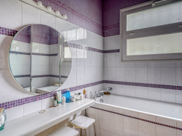 Bathroom with bathtub, round mirror and white and purple tiles.