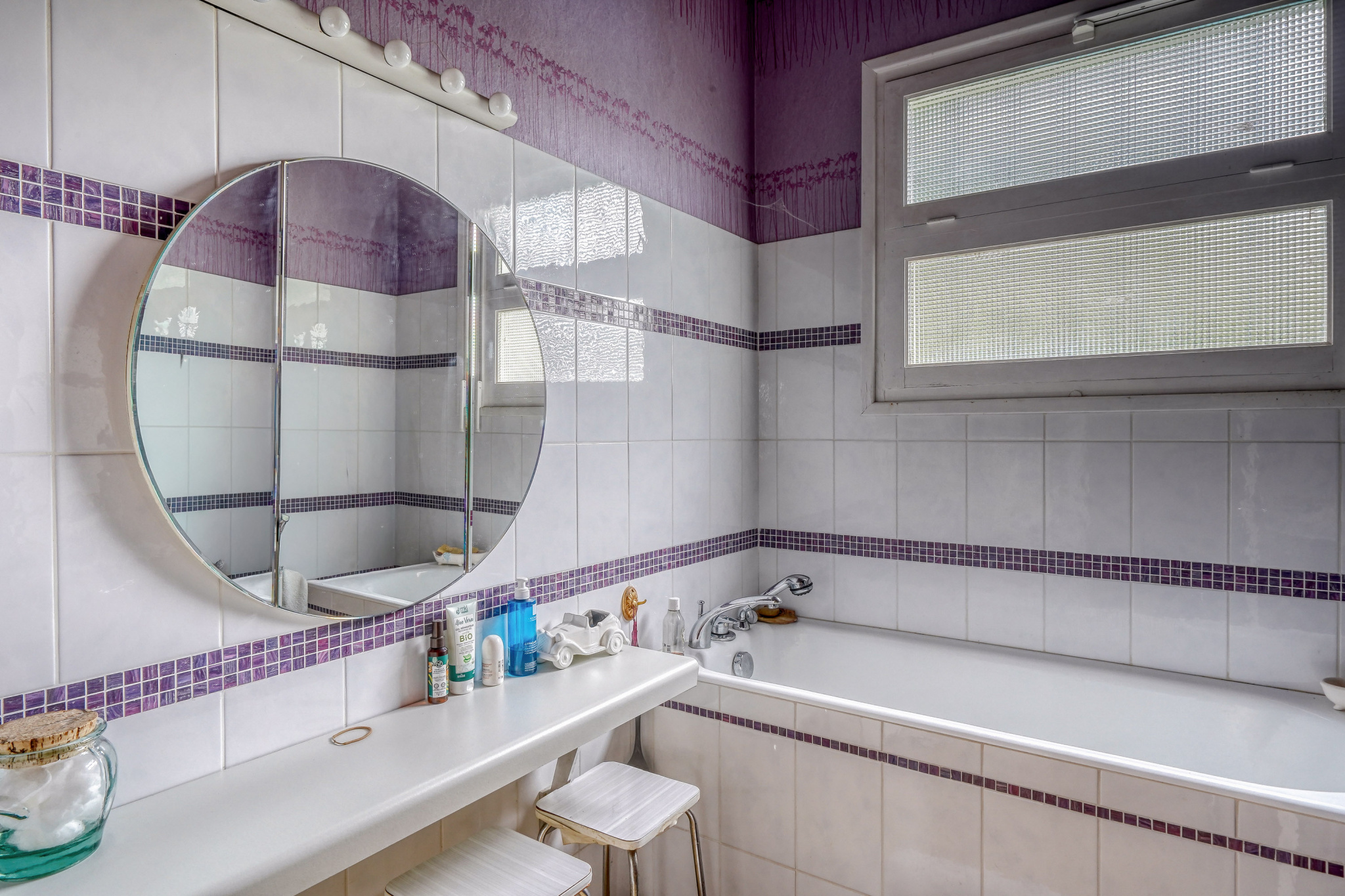 Bathroom in a house in La Teste-de-Buch Bathroom with bathtub, round mirror and white and purple tiles.