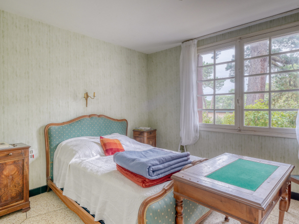 Room in a house to be renovated with bed, table and window overlooking the outside.