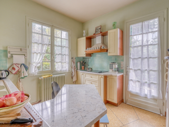 Kitchen of a traditional house with light-colored furniture and windows overlooking the outside.