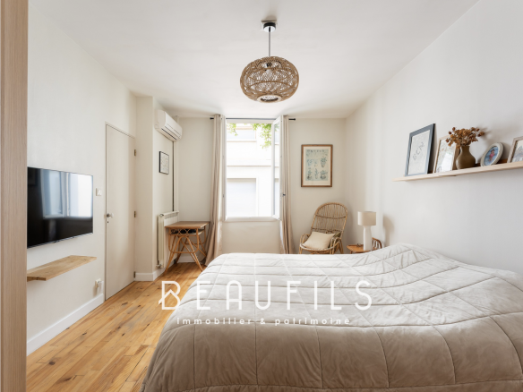 Chambre d'une maison rénovée à Montpellier avec un lit, un fauteuil et une télévision murale.
