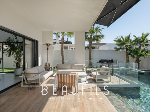 Terrace of a contemporary villa with swimming pool and outdoor furniture, surrounded by palm trees.