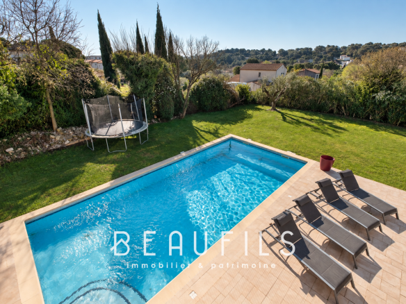 View of a villa with swimming pool and sun loungers, green garden in the background.