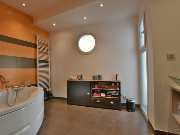 Salle de bain moderne avec baignoire et rangement, murs orange et blancs.