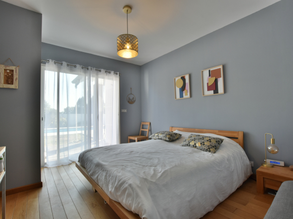 Chambre lumineuse avec un lit double et accès à l'extérieur, piscine visible par la fenêtre.