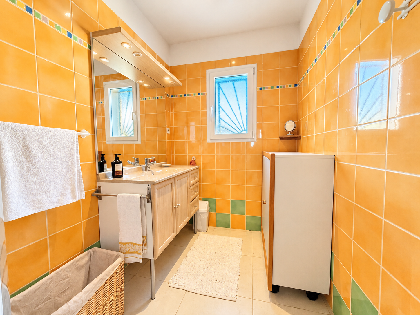 Salle de bain de maison à Saint-Sériès Salle de bain lumineuse avec carrelage orange et meuble vasque, fenêtres avec volets.