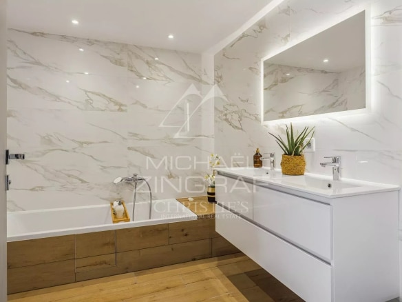 Salle de bain moderne avec baignoire et meuble sous vasque en bois, murs en marbre.