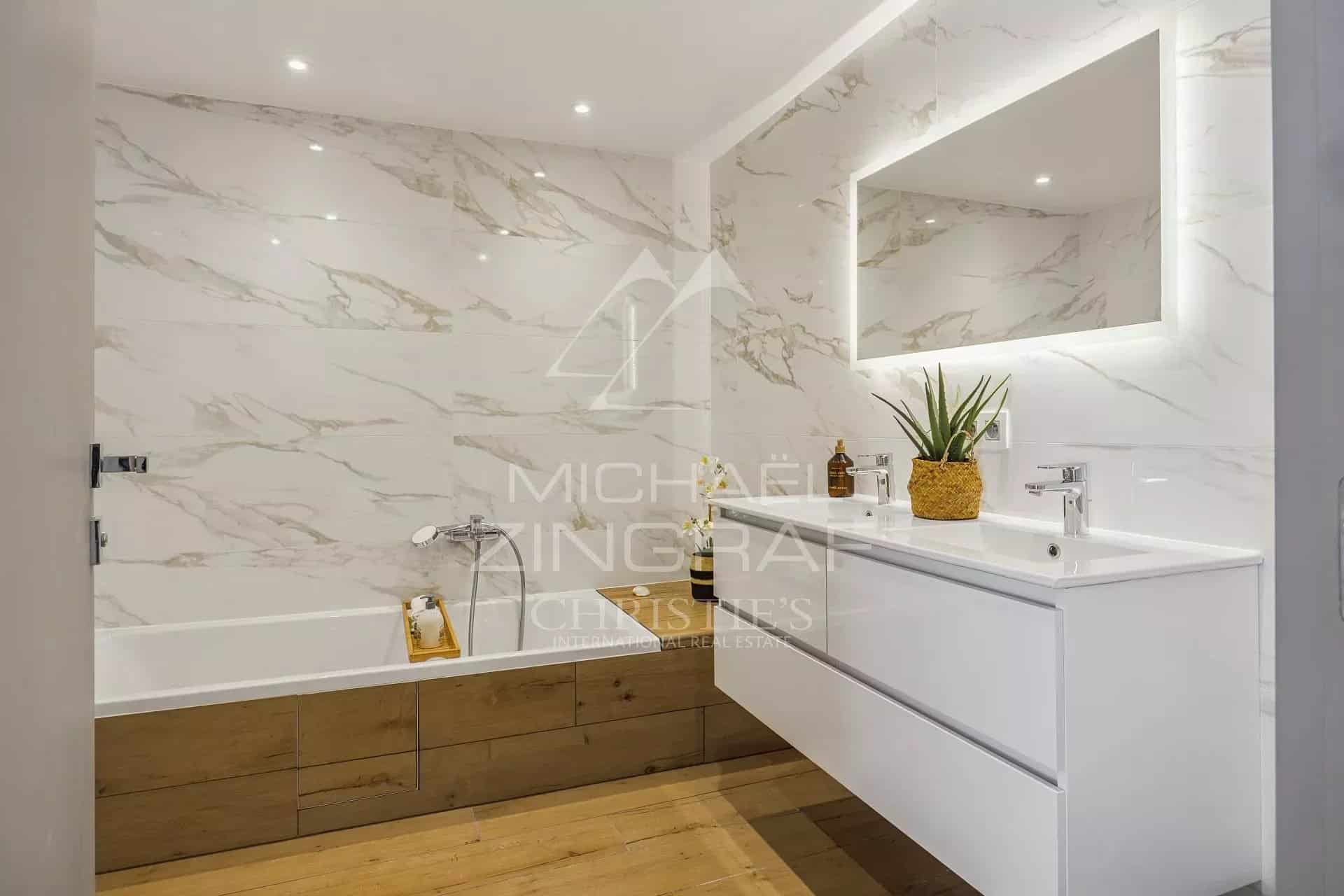Salle de bain moderne avec baignoire et meuble sous vasque en bois, murs en marbre.