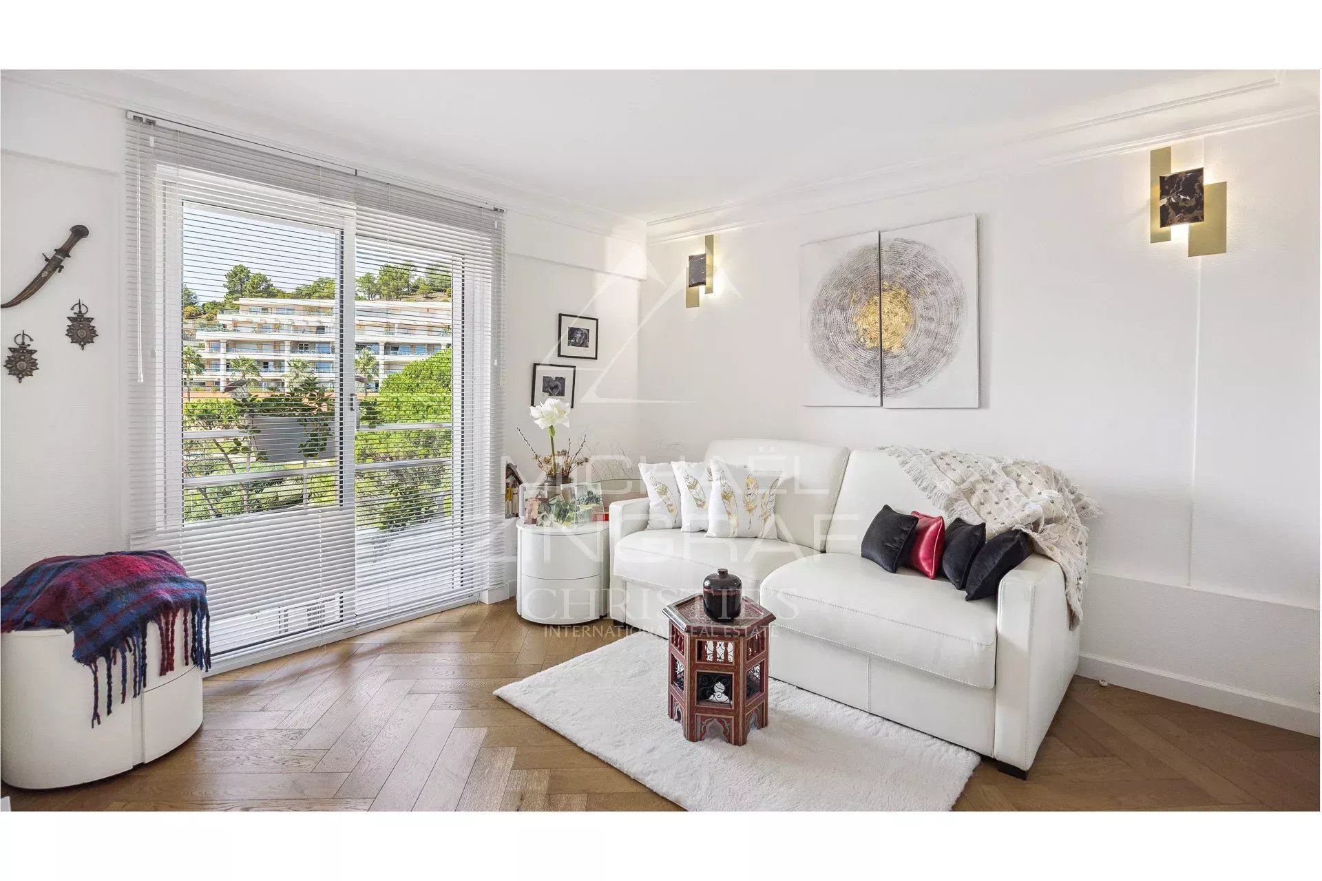 Salon d'un appartement rénové avec canapé blanc et décoration moderne, vue sur la nature.
