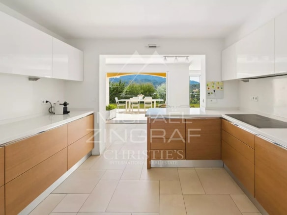 Modern kitchen with wood and white furniture, overlooking the terrace and garden.