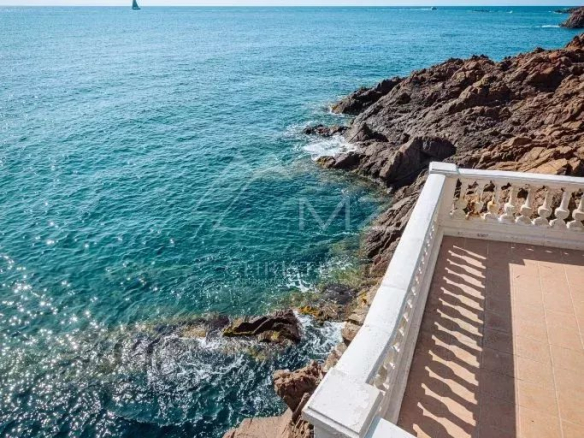 Vue sur la mer depuis une villa Art Déco à Anthéor, avec des rochers et un bateau à voile au loin.