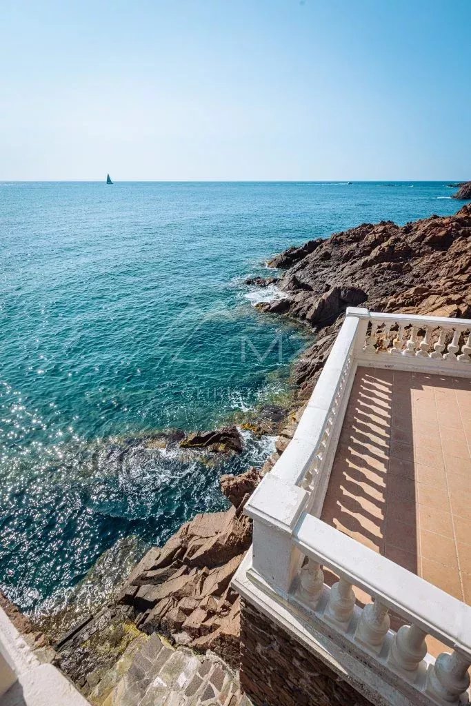 Vue sur la mer depuis une villa Art Déco à Anthéor, avec des rochers et un bateau à voile au loin.