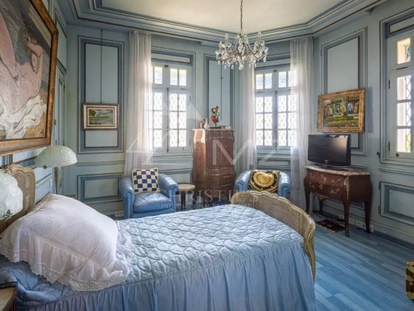 Chambre d'une villa Art Déco à Anthéor, avec murs bleus et fenêtres lumineuses.