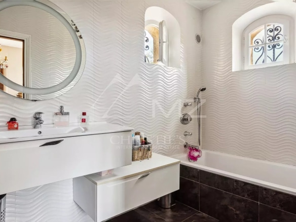 Salle de bain moderne avec baignoire et lavabo, murs ondulés, fenêtre avec grille décorative.