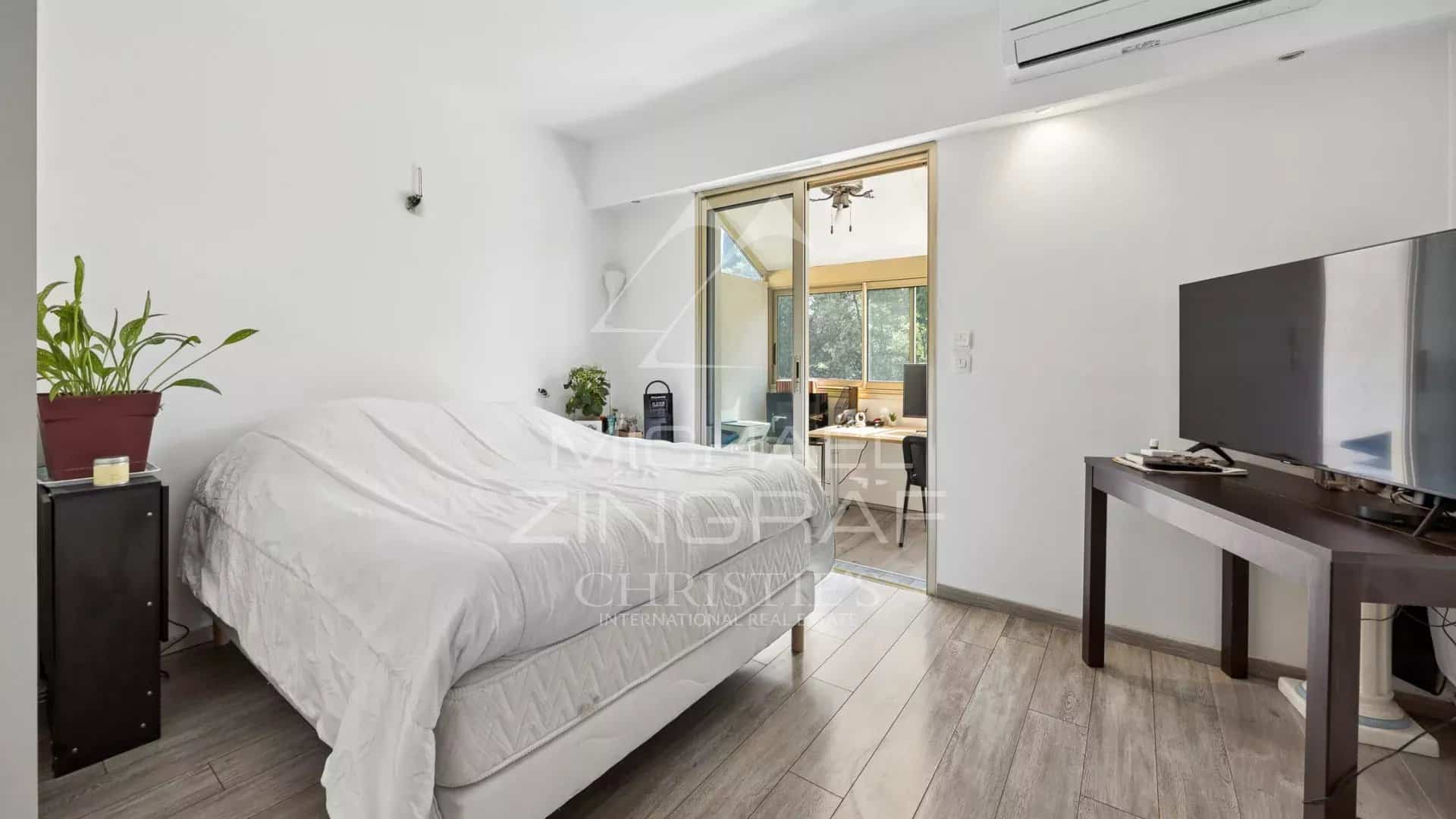 Chambre d'un appartement avec lit, télévision et accès à un balcon.