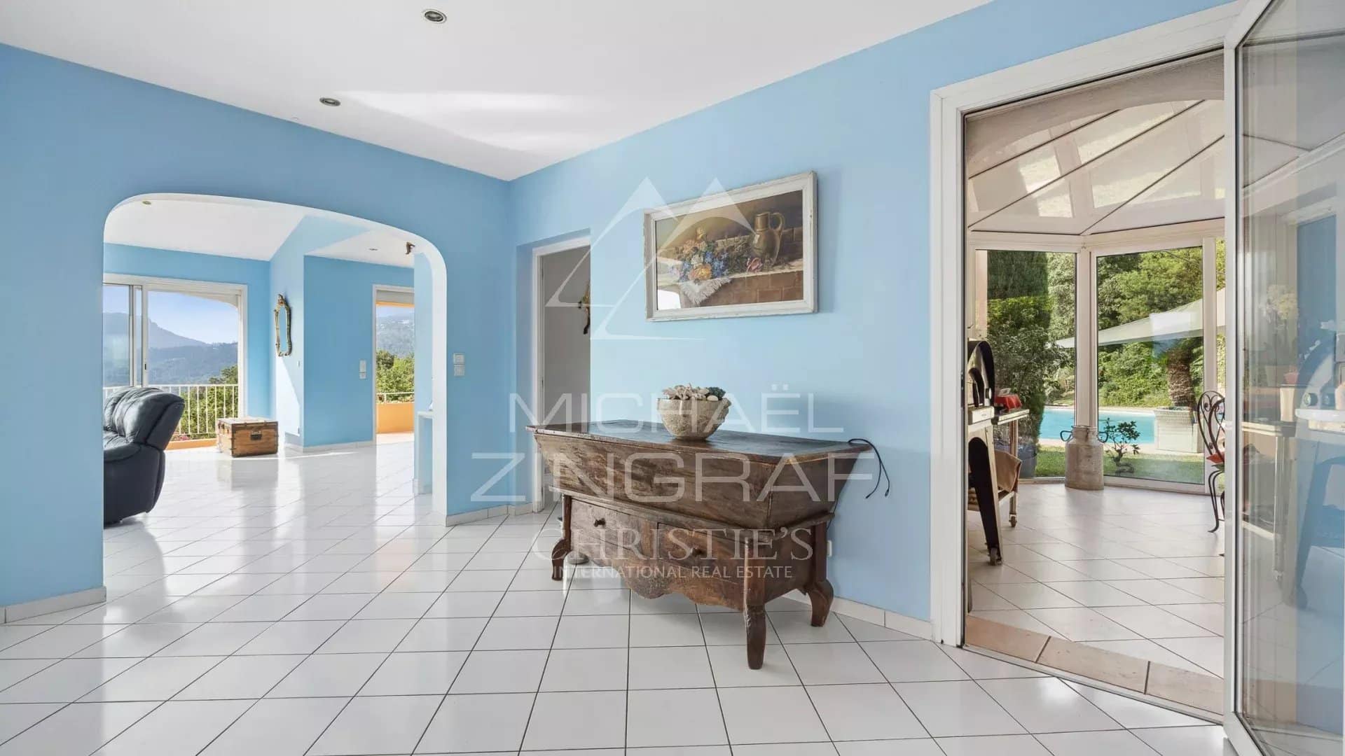 Interior of a bright villa with blue walls and white tiles, overlooking nature.