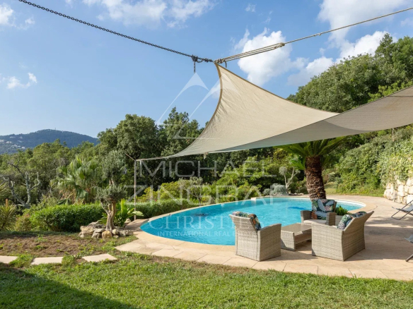 Outdoor area of ​​a villa with swimming pool, chairs and shade sails, surrounded by greenery.