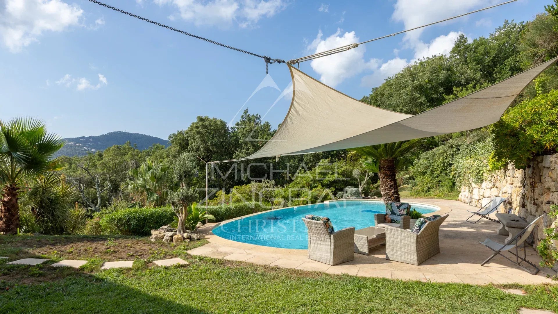 Outdoor area of ​​a villa with swimming pool, chairs and shade sails, surrounded by greenery.