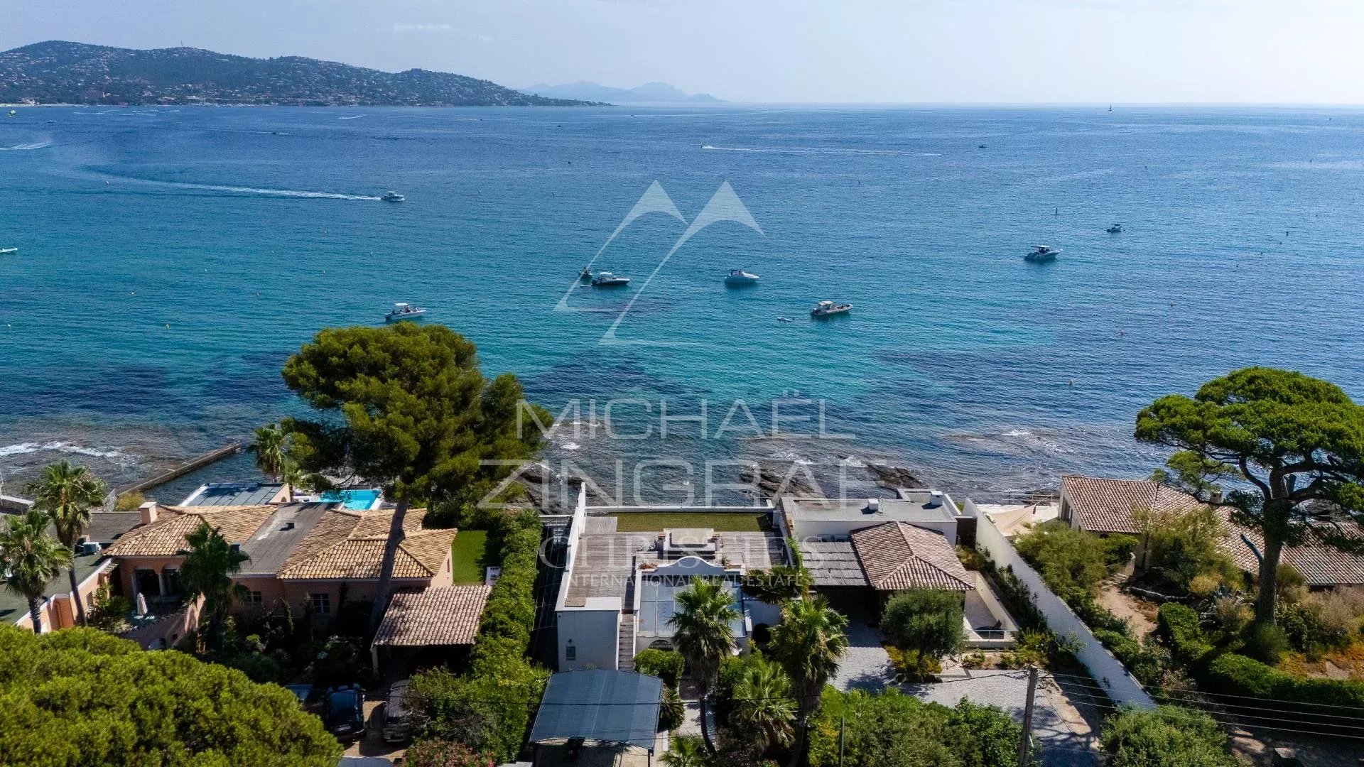 Vue aérienne d'une villa en bord de mer à Sainte-Maxime, entourée de végétation et de bateaux sur l'eau.