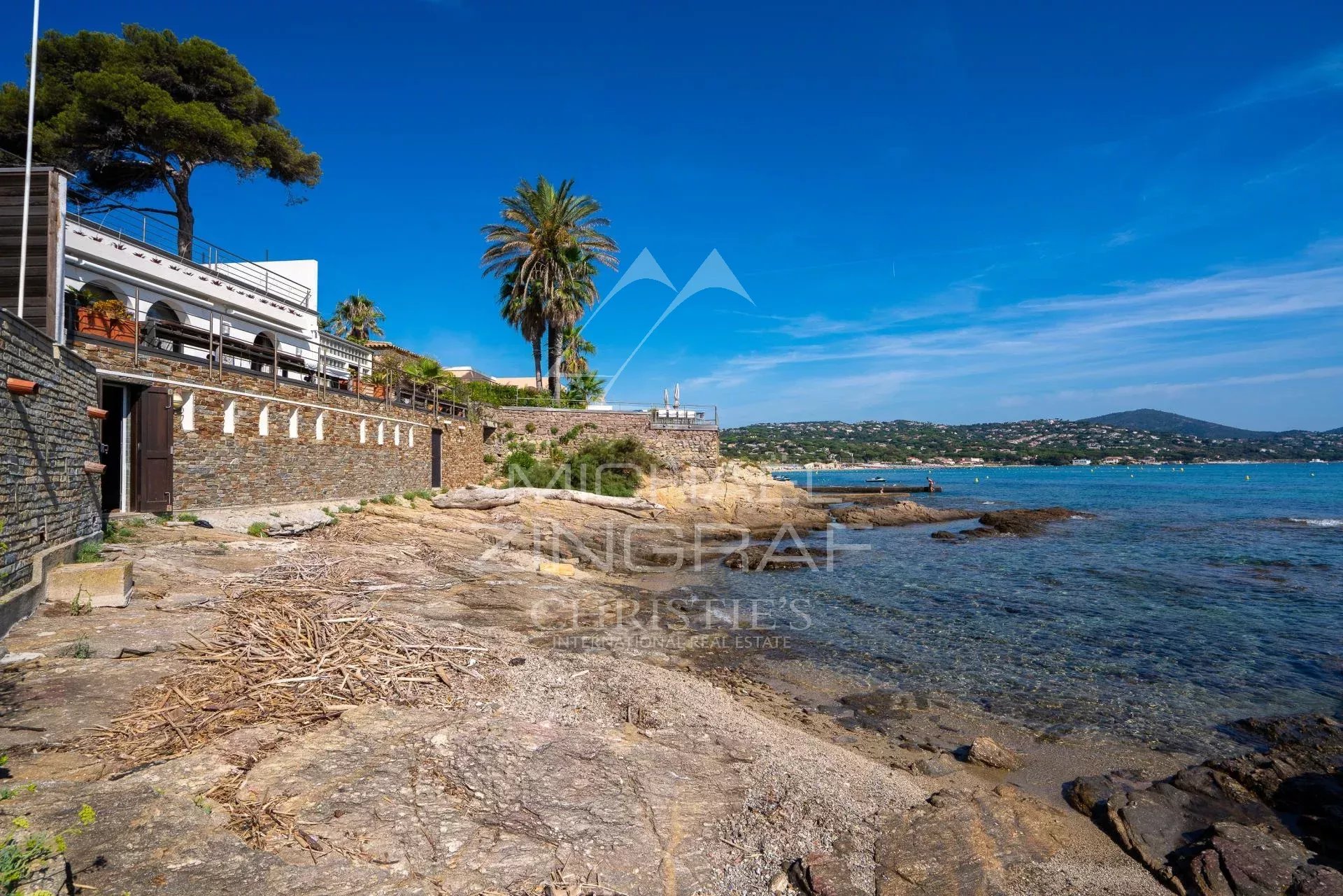 Vue de la villa en bord de mer à Sainte-Maxime, avec des rochers et la mer en arrière-plan.