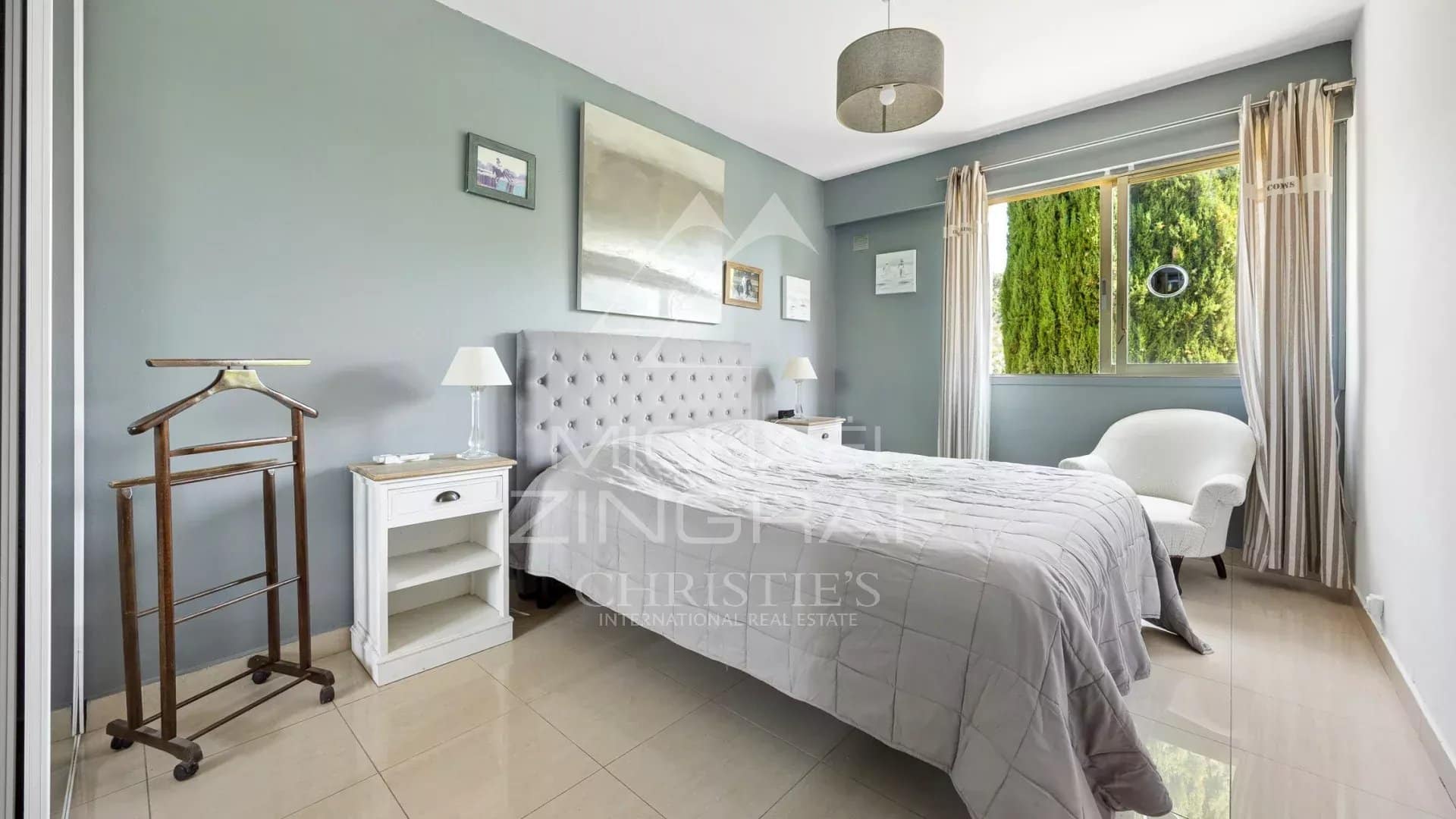 Chambre lumineuse avec lit double et décoration sobre, fenêtres donnant sur un jardin verdoyant.