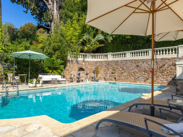 Swimming pool with sun loungers and parasol in a villa in Théoule-sur-Mer, surrounded by greenery.