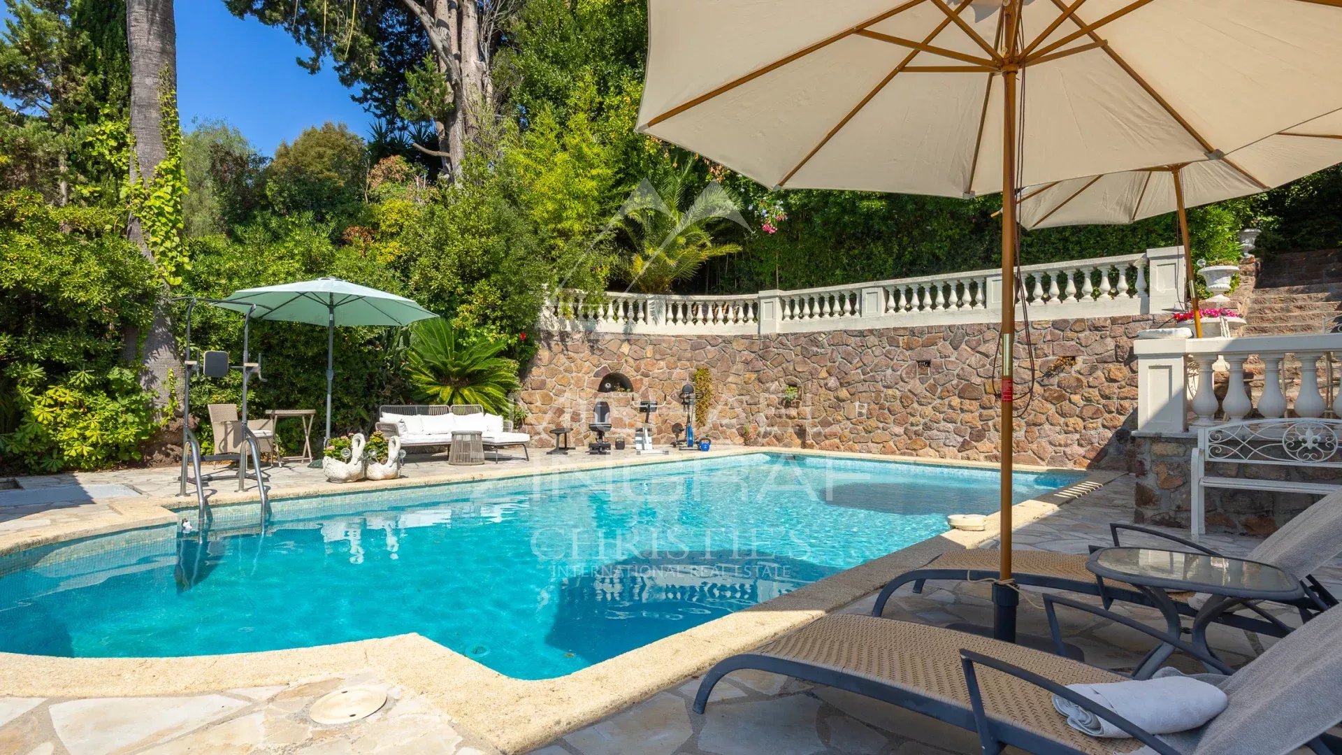 Villa with swimming pool in Théoule-sur-Mer Swimming pool with sun loungers and parasol in a villa in Théoule-sur-Mer, surrounded by greenery.