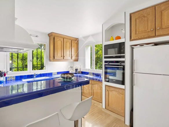 Cuisine moderne avec meubles en bois et carrelage bleu, ouverte sur l'extérieur.