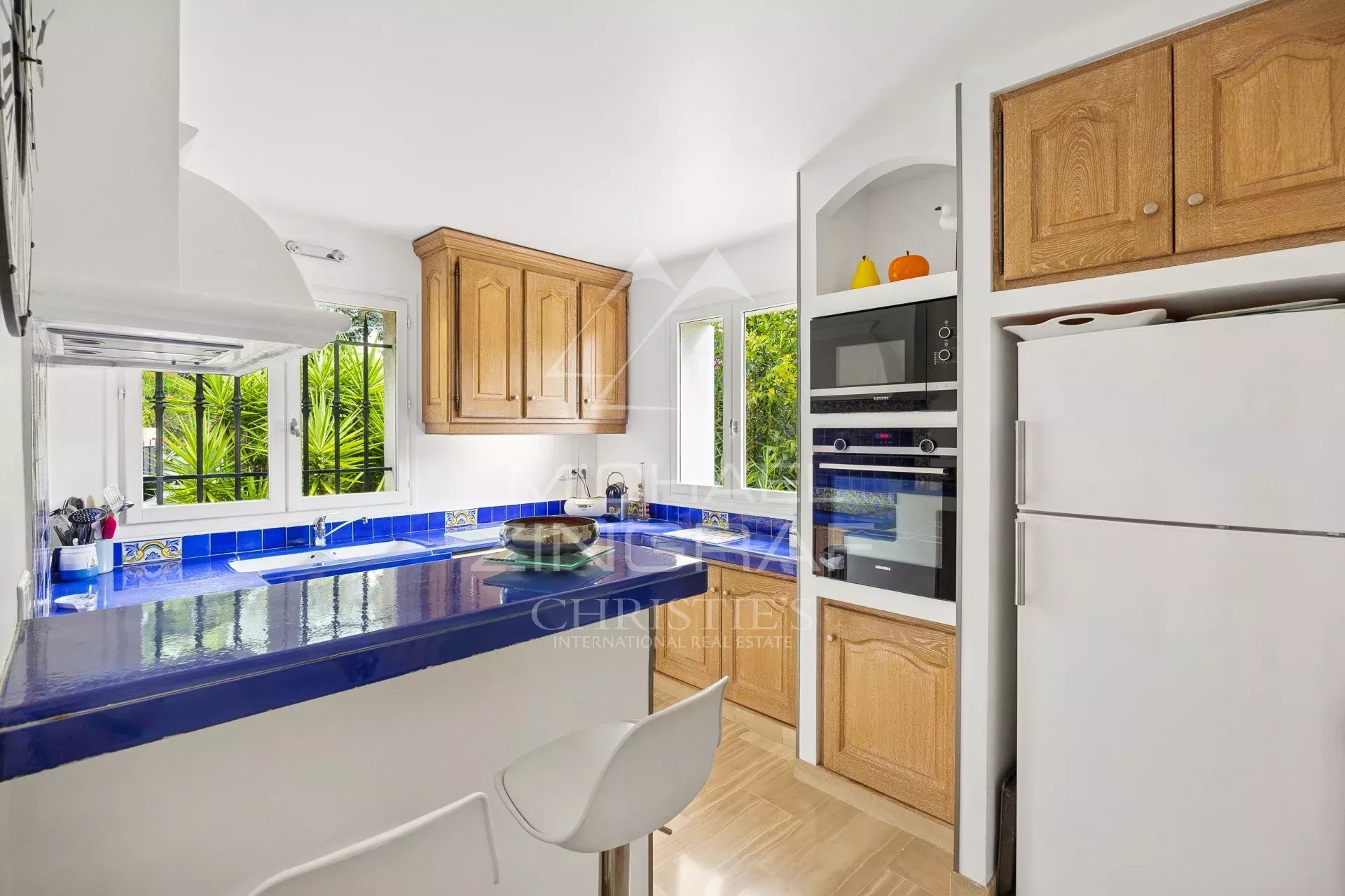 Cuisine d’une maison à Mandelieu-la-Napoule Cuisine moderne avec meubles en bois et carrelage bleu, ouverte sur l'extérieur.