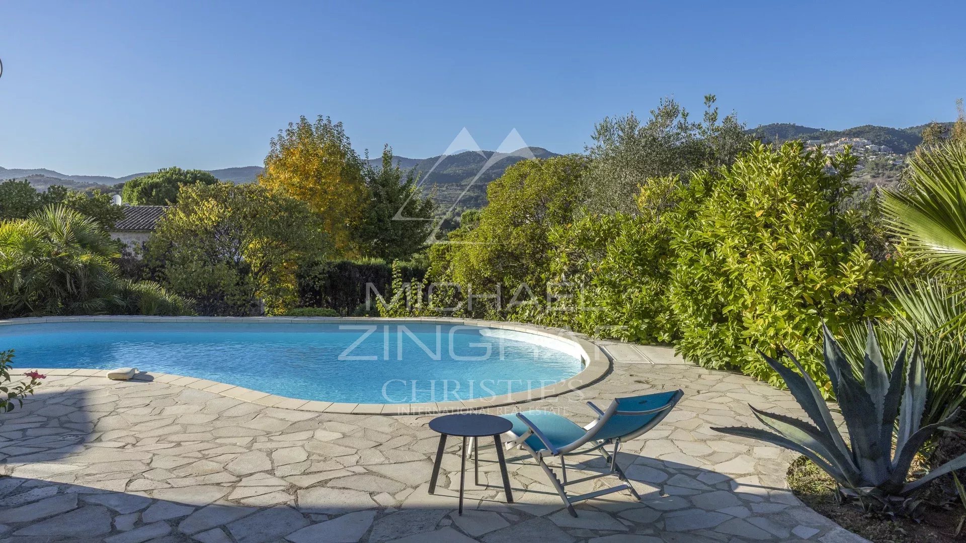 View of the pool and garden of a family home in Mandelieu-La Napoule with mountains in the background.