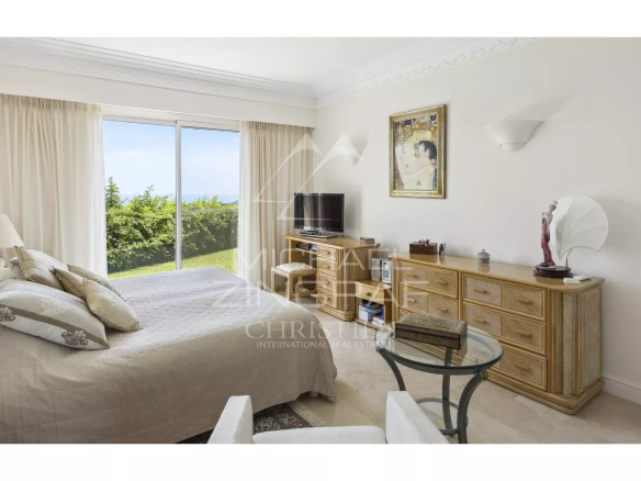 Chambre d'une villa avec vue sur la mer, mobilier élégant et accès à un jardin.