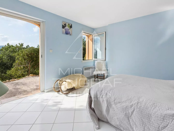 Chambre lumineuse avec vue sur la nature, murs peints en bleu et accès à l'extérieur.