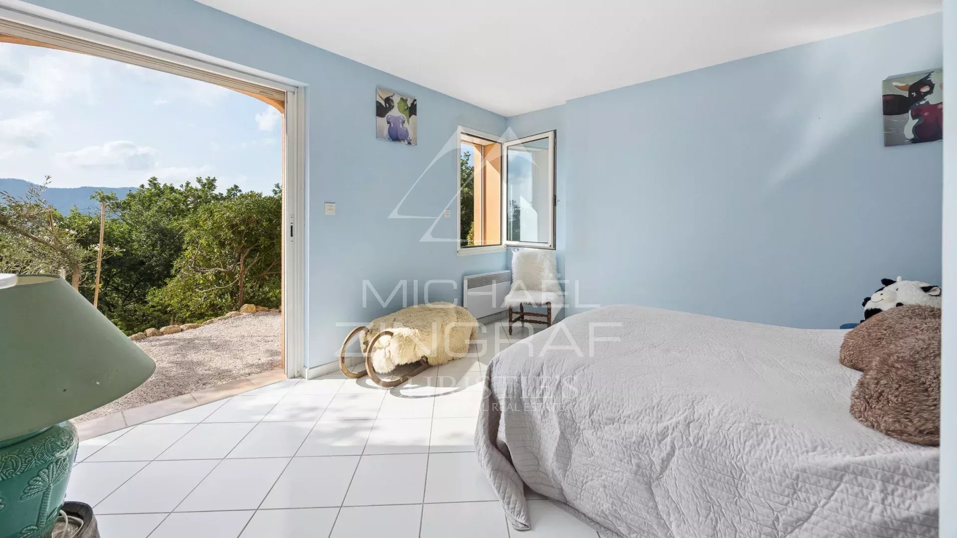 Chambre avec vue dans une propriété Chambre lumineuse avec vue sur la nature, murs peints en bleu et accès à l'extérieur.