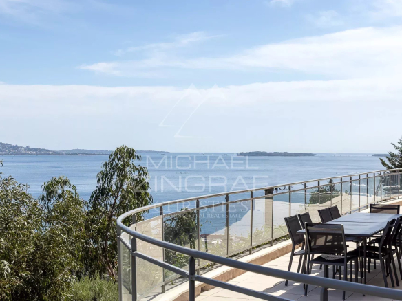 Vue mer depuis une terrasse avec une table et des chaises, entourée de verdure.