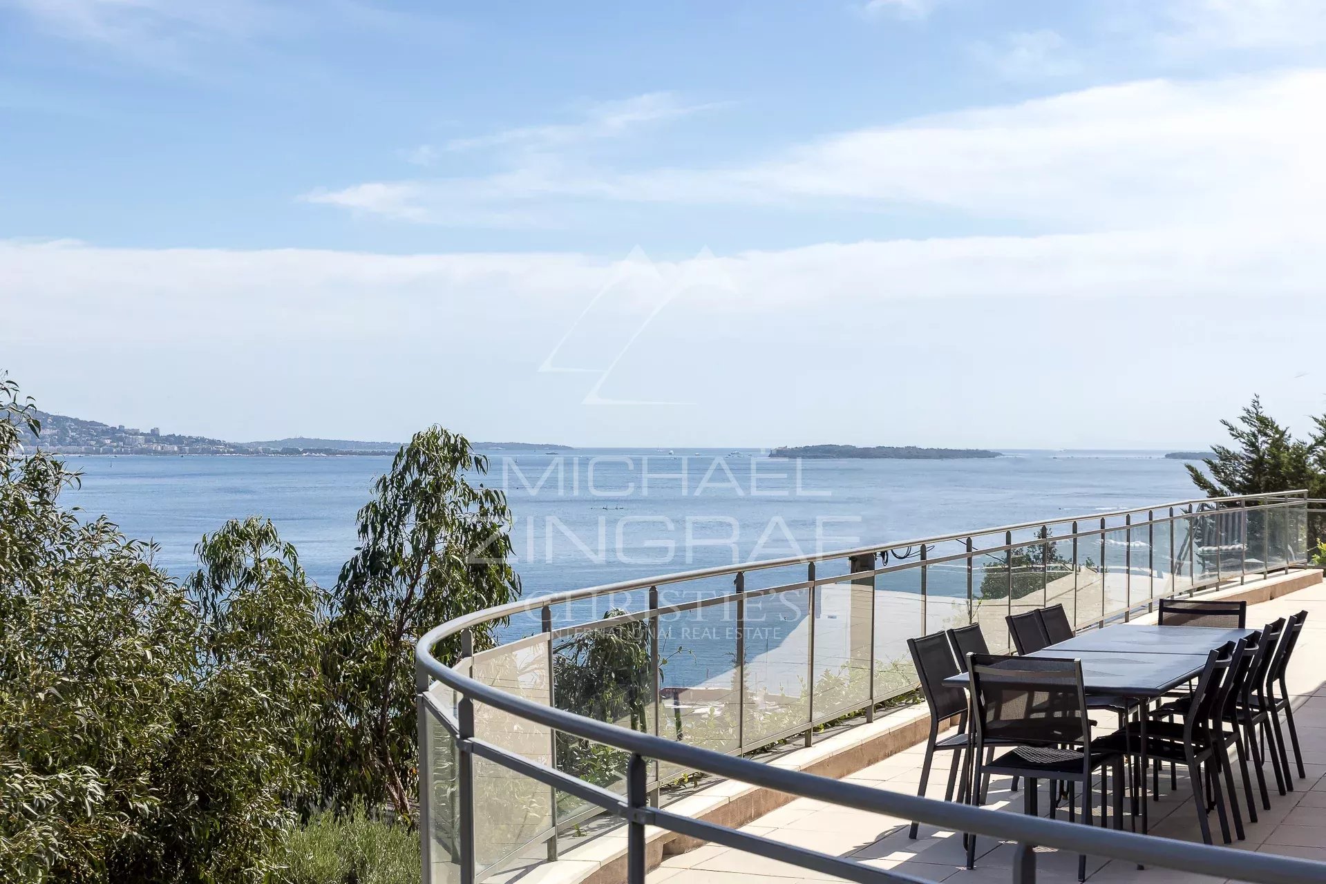 Terrasse avec vue sur la mer à Théoule-sur-Mer Vue mer depuis une terrasse avec une table et des chaises, entourée de verdure.