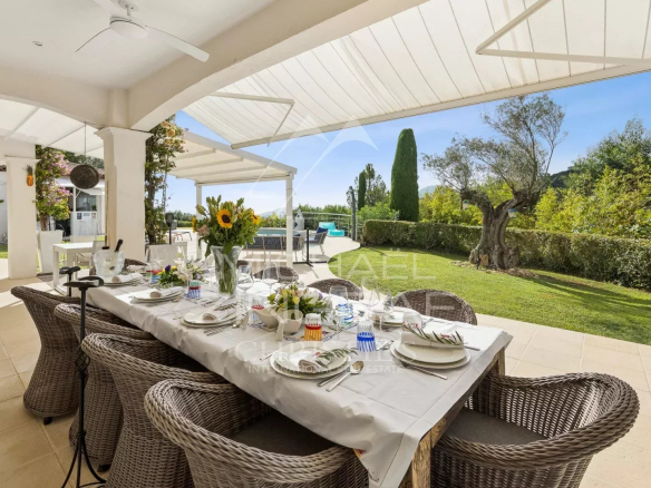 Terrasse d'une propriété avec table dressée et vue sur un jardin verdoyant et la mer.