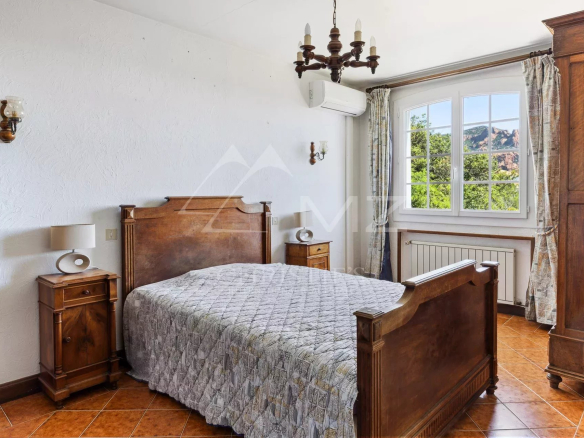 Chambre avec lit en bois et fenêtre donnant sur la végétation et les roches rouges d'Anthéor.