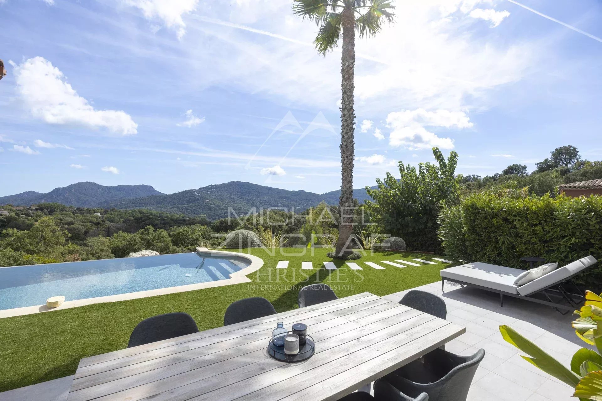 Vue de la terrasse d'une villa contemporaine avec piscine et jardin, entourée de collines verdoyantes.