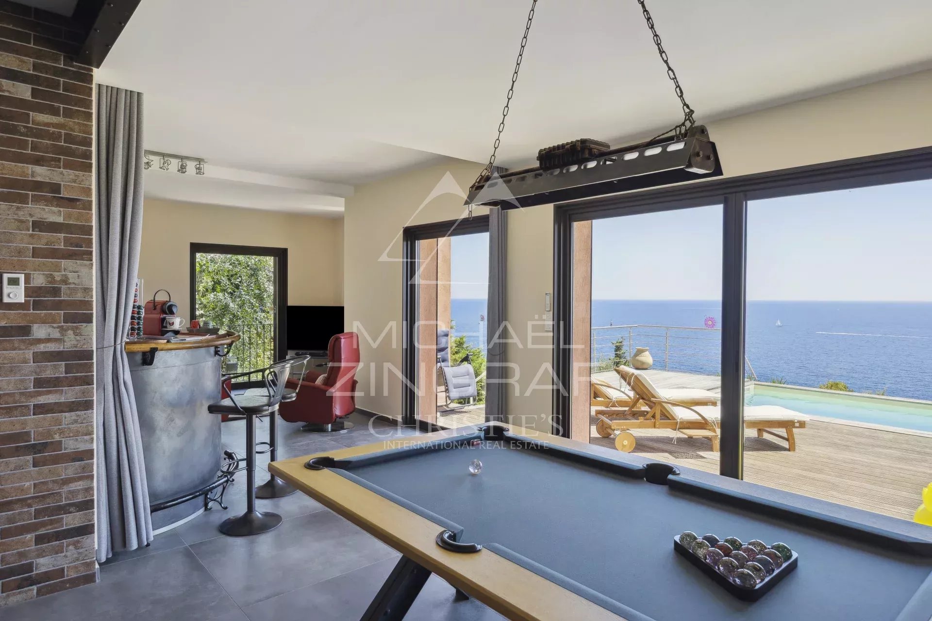 Intérieur d'une propriété rénovée avec vue mer, billard et accès à une terrasse.
