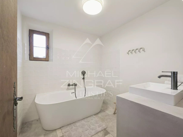 Salle de bain moderne avec baignoire et lavabo, murs blancs et fenêtre.